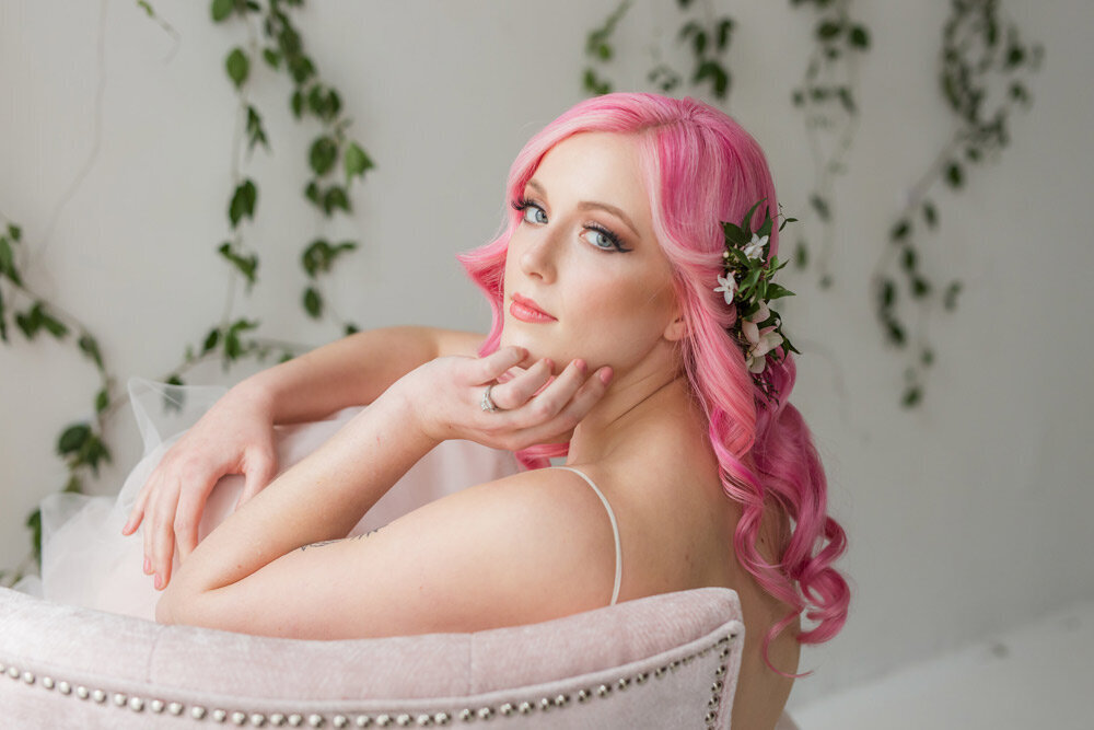 Bride with long, newly styled pink hair poses in a a chair