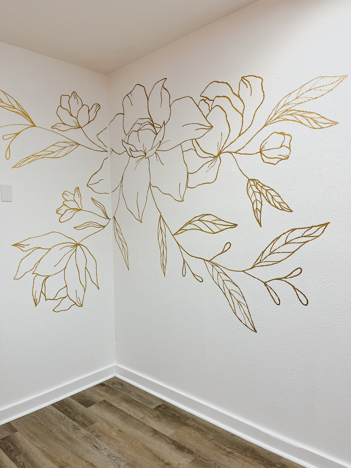 A corner in a salon featuring a white wall with custom florals in gold drawn on it representing full service design and calligraphy by Life in Letters.