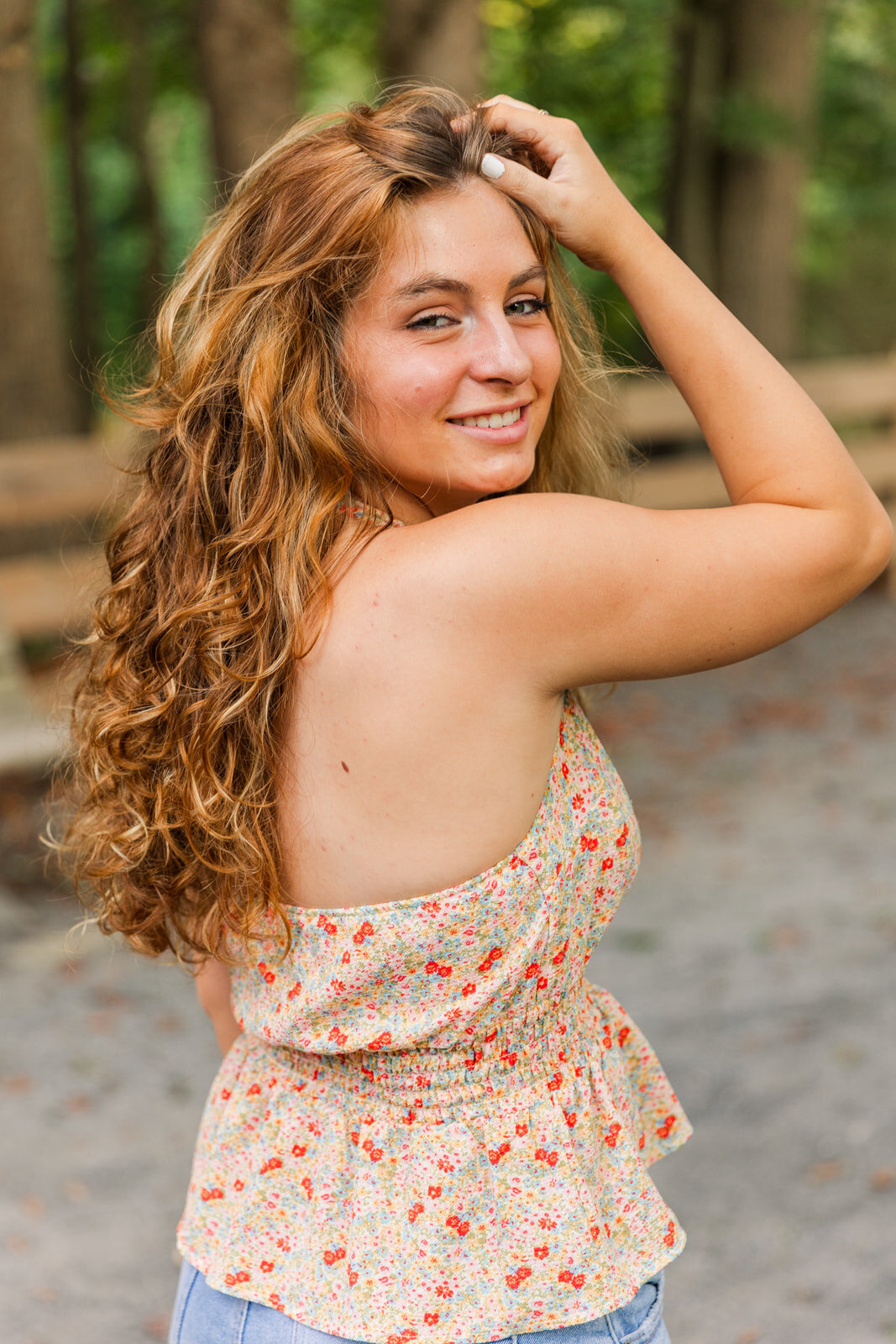 senior girl in flowery toplooking above her shoulder her hand on the hair in an Atlanta park