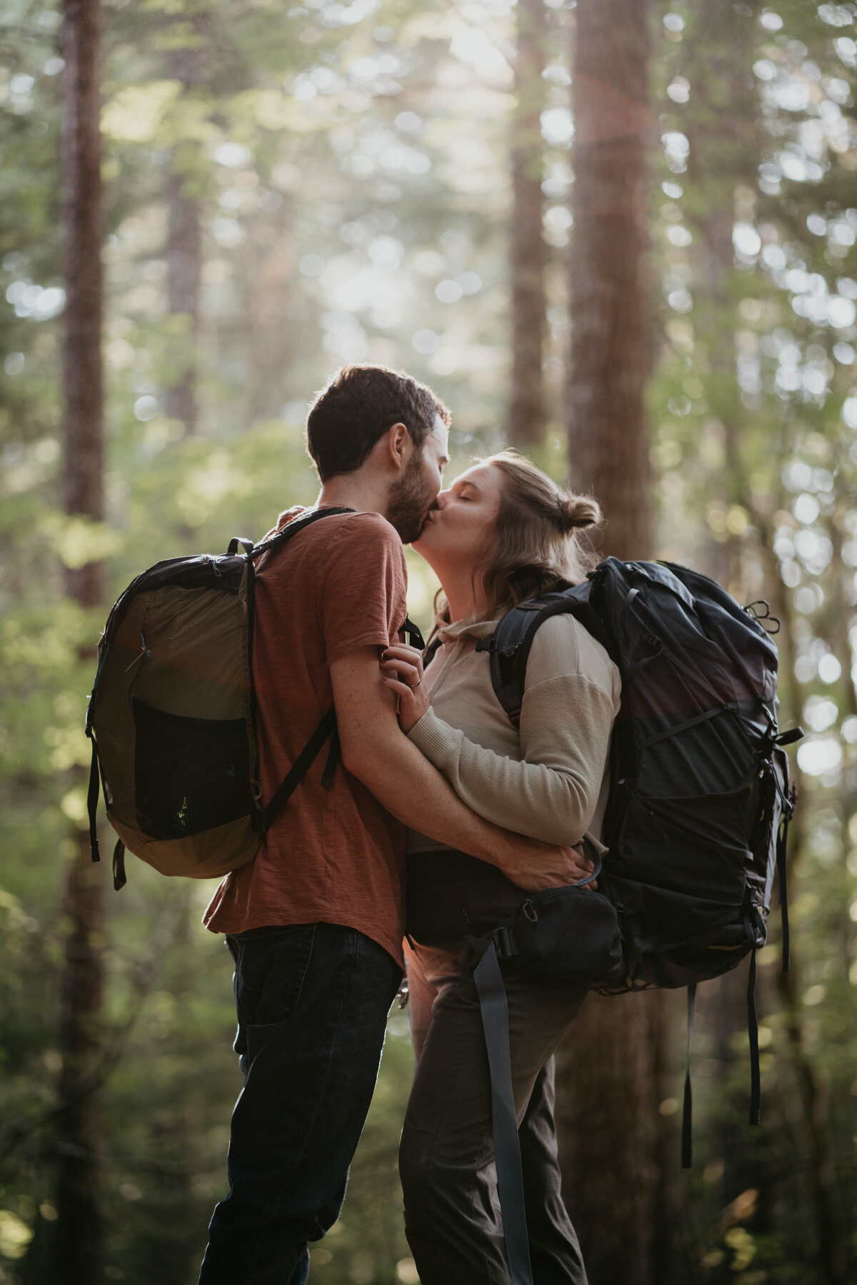 Couple kissing with backpacks while hiking to rock climbing engagement photos