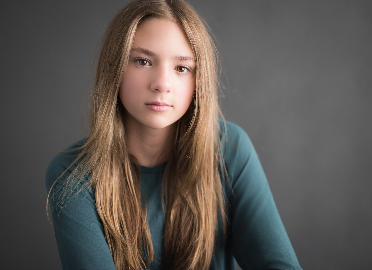 teen with long straight blonde hair and teal shirt in studio portrait