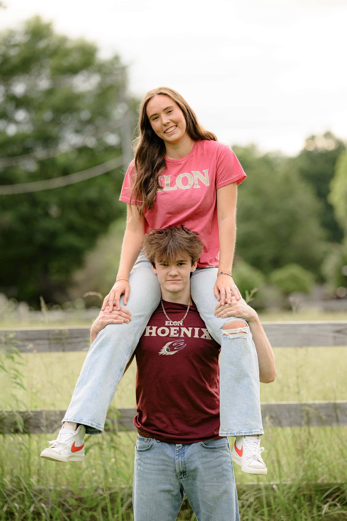 twin sibling seniors sit with girl on brother shoulders wearing college t shirts