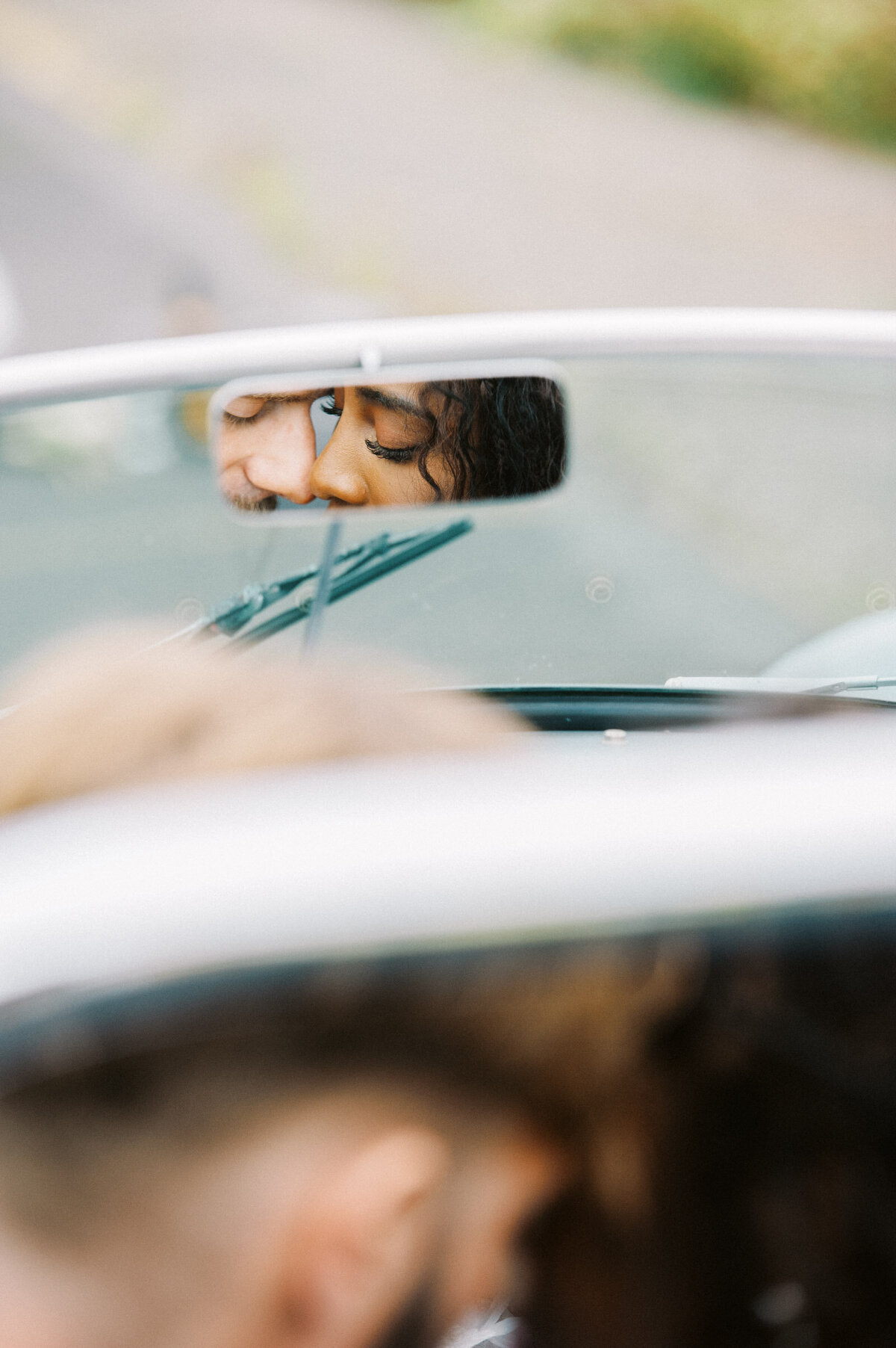 bi_racial couple kissing in the rear view mirror of their vintage convertible