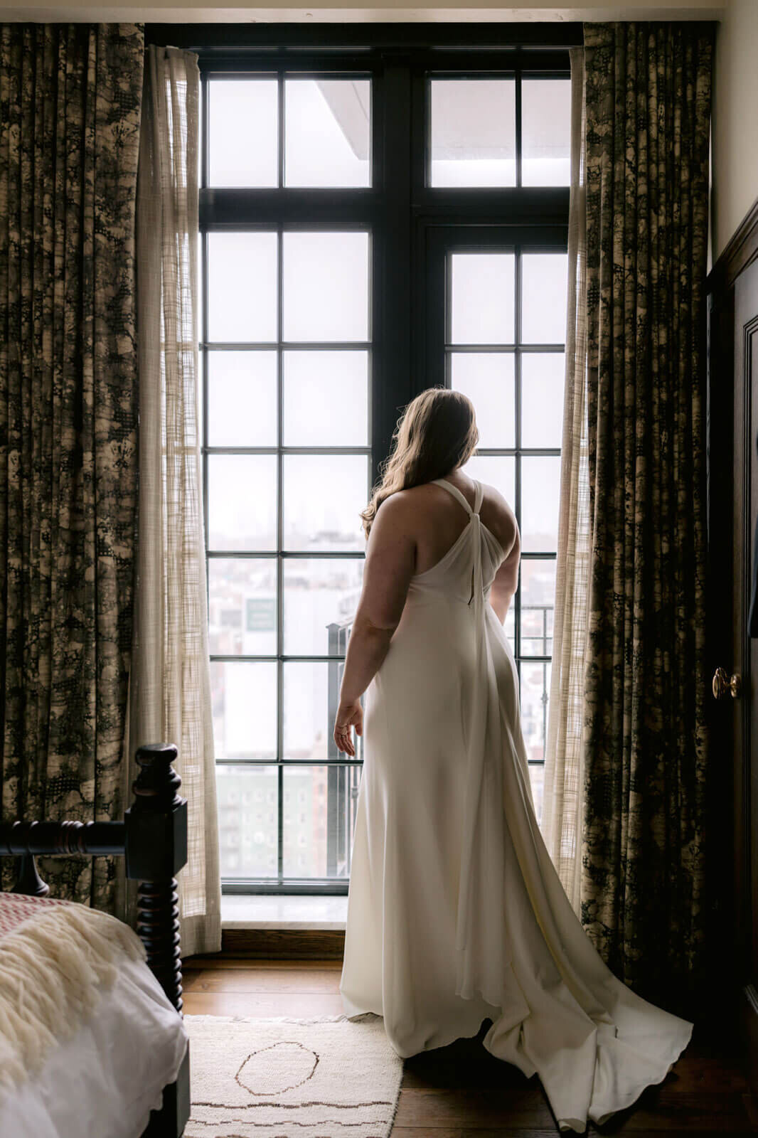 Back view of the bride looking out the huge window in a Ludlow Hotel room.
