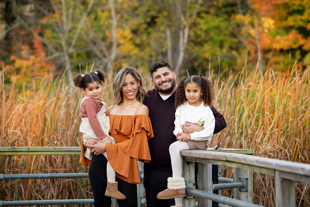 Mom and dad with their two daughters standing on a bridge for their family photos in Burlington, ON