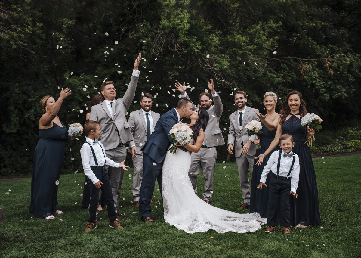 Joyous wedding celebration with bridal party and guests throwing petals as the happy couple shares a romantic kiss taken by jen Jarmuzek photography a Minneapolis wedding photographer