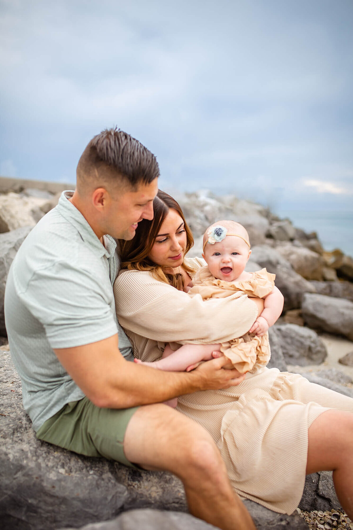 Clearwater FL beach family portrait sitting on the rocks while father and mother cuddle the little girl 