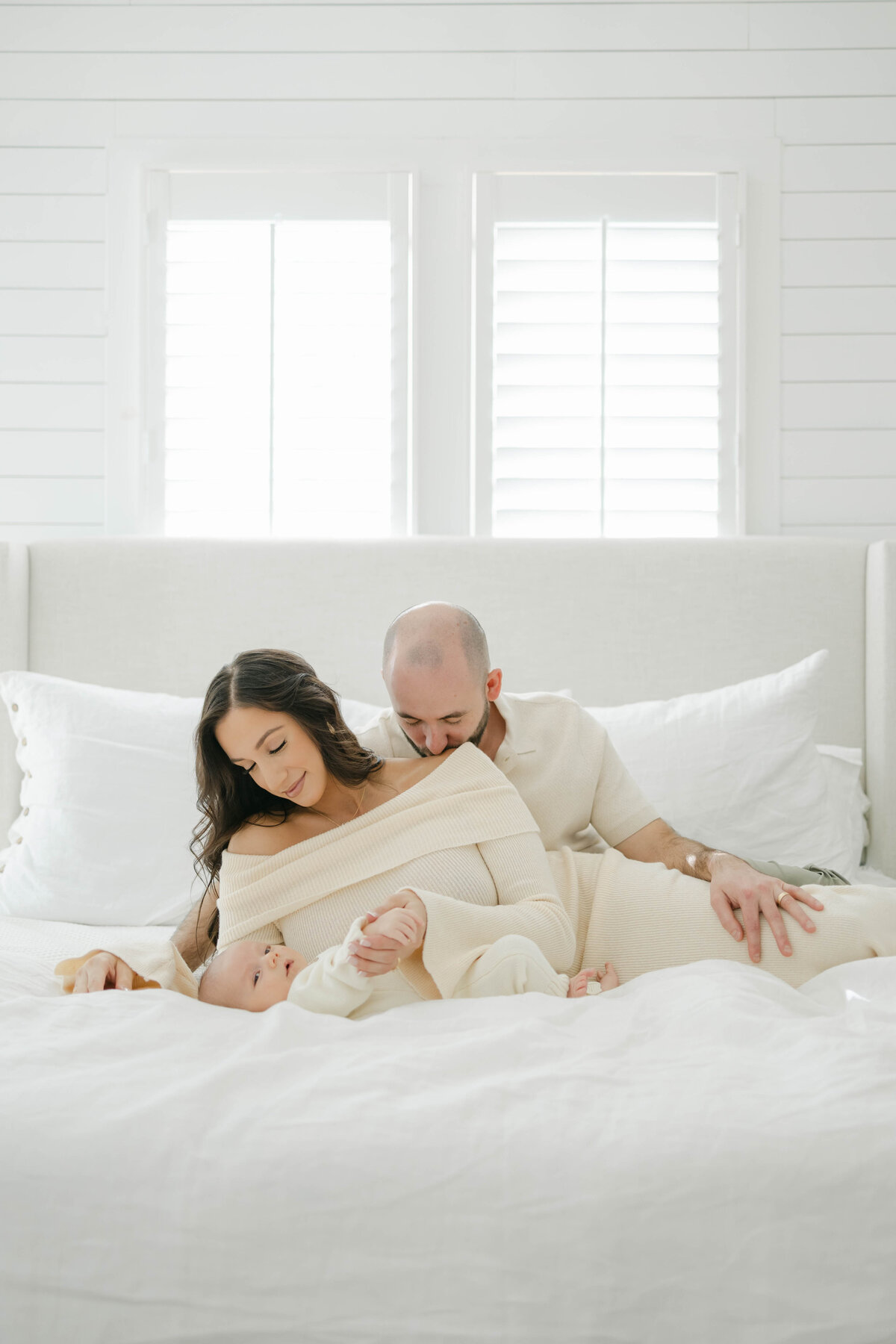 a couple laying in bed looking at their newborn baby boy in a white room in a dallas texas home