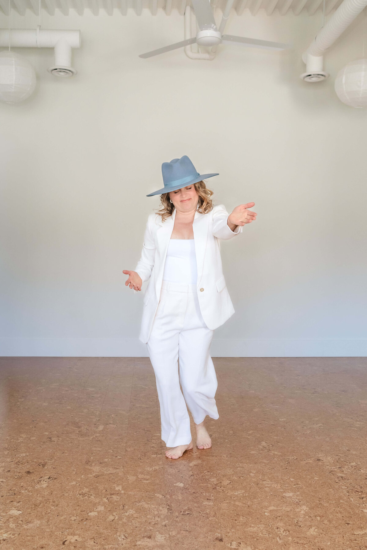 professional business portrait of stylish woman in cream suit and blue hat dancing