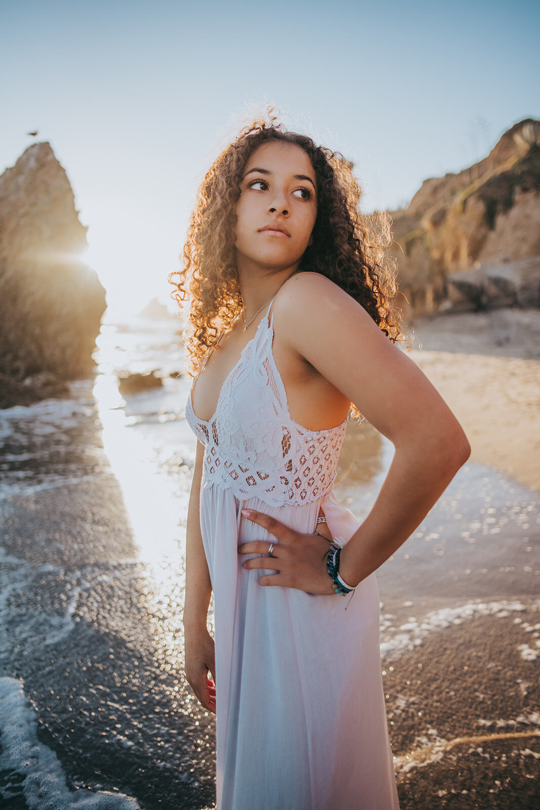 Olivia wears a white dress on El Matador beach during sunset and stares into the distance.
