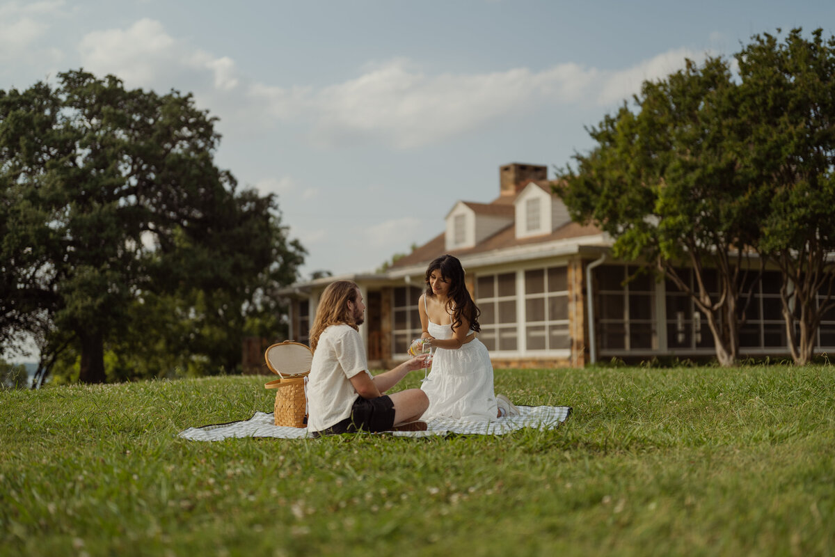 A unique engagement portrait featuring the couple sitting with a historic house backdrop near White Rock Lake.