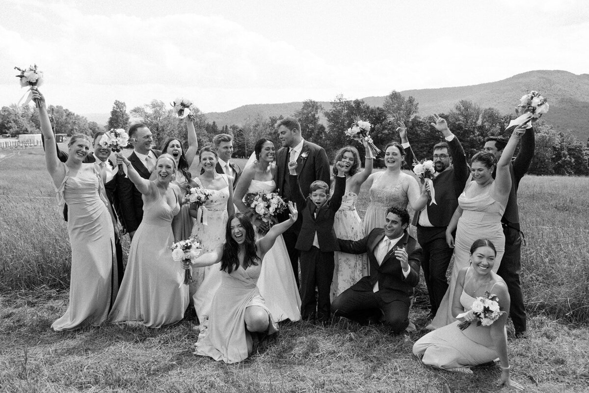 A black and white photo of a wedding party cheering on the bride and groom with Vermont mountains in the background.