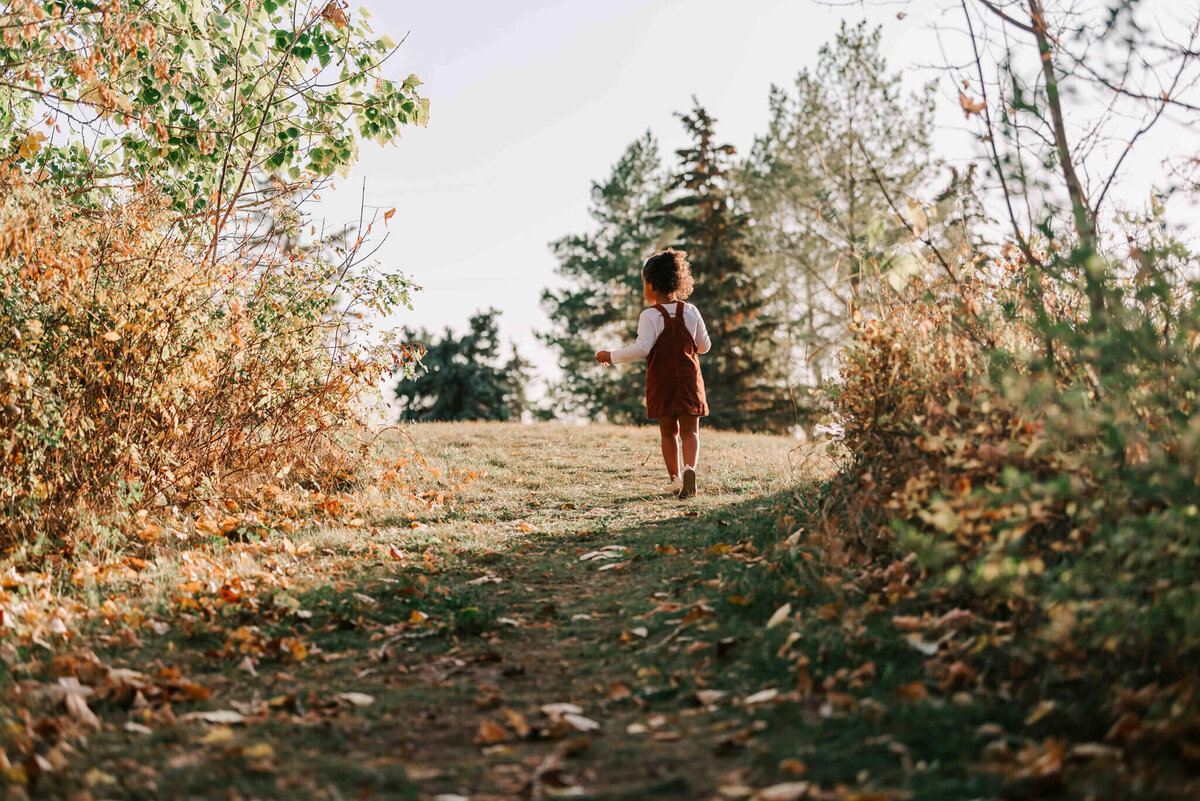 The little girl walking down a path with her back tot he camera. 