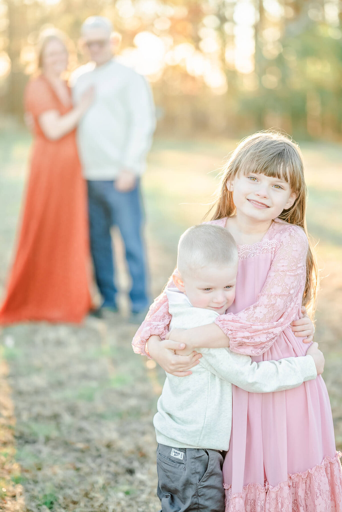 A brother and sister hug while standing in front of their mom and dad during a family session in Hampton Roads