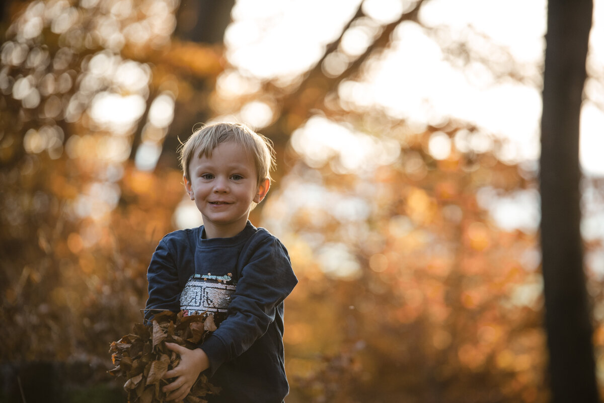 Junge spielt mit Laub im Wald Herbstlaub