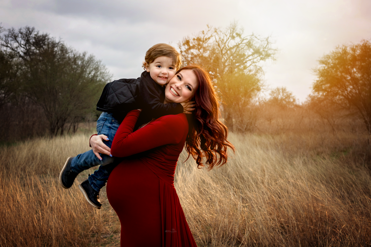 Elevate your maternity experience with an elegant winter session near San Antonio. Our mom-to-be, in a scarlet flying dress, adds fiery elegance to the winter field backdrop.