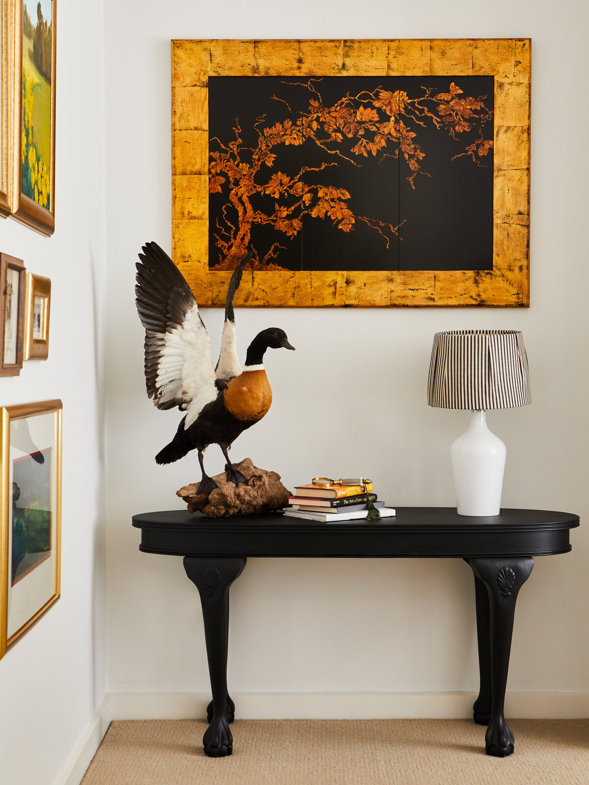 An entryway console table in a home in Eynesbury featuring a taxidermy bird sculpture. A large framed artwork with a gold botanical pattern on a black background hangs on the wall behind it.