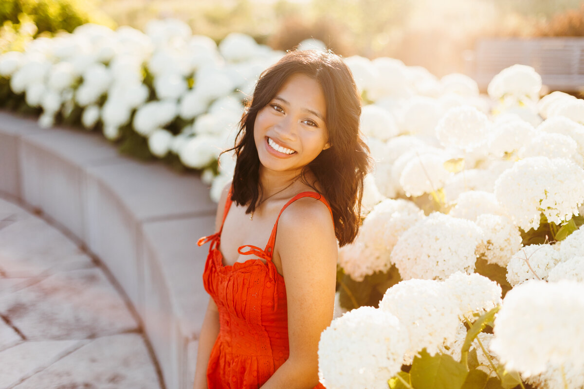 Senior girl in a red top posing in front of white hydrangea bushes