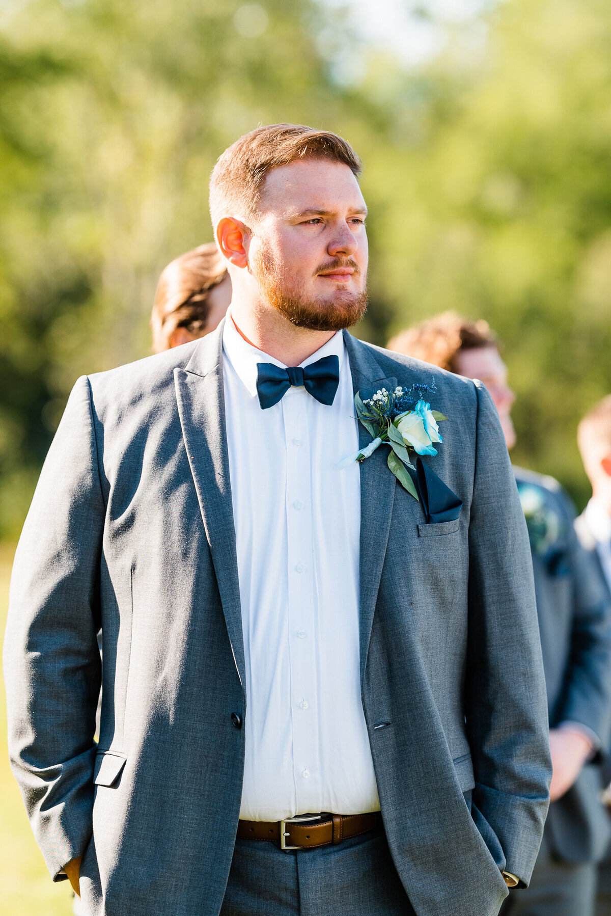groom standing with his hands in his pockets and looking down the aisle to see his brides entrance to their outdoor wedding ceremony