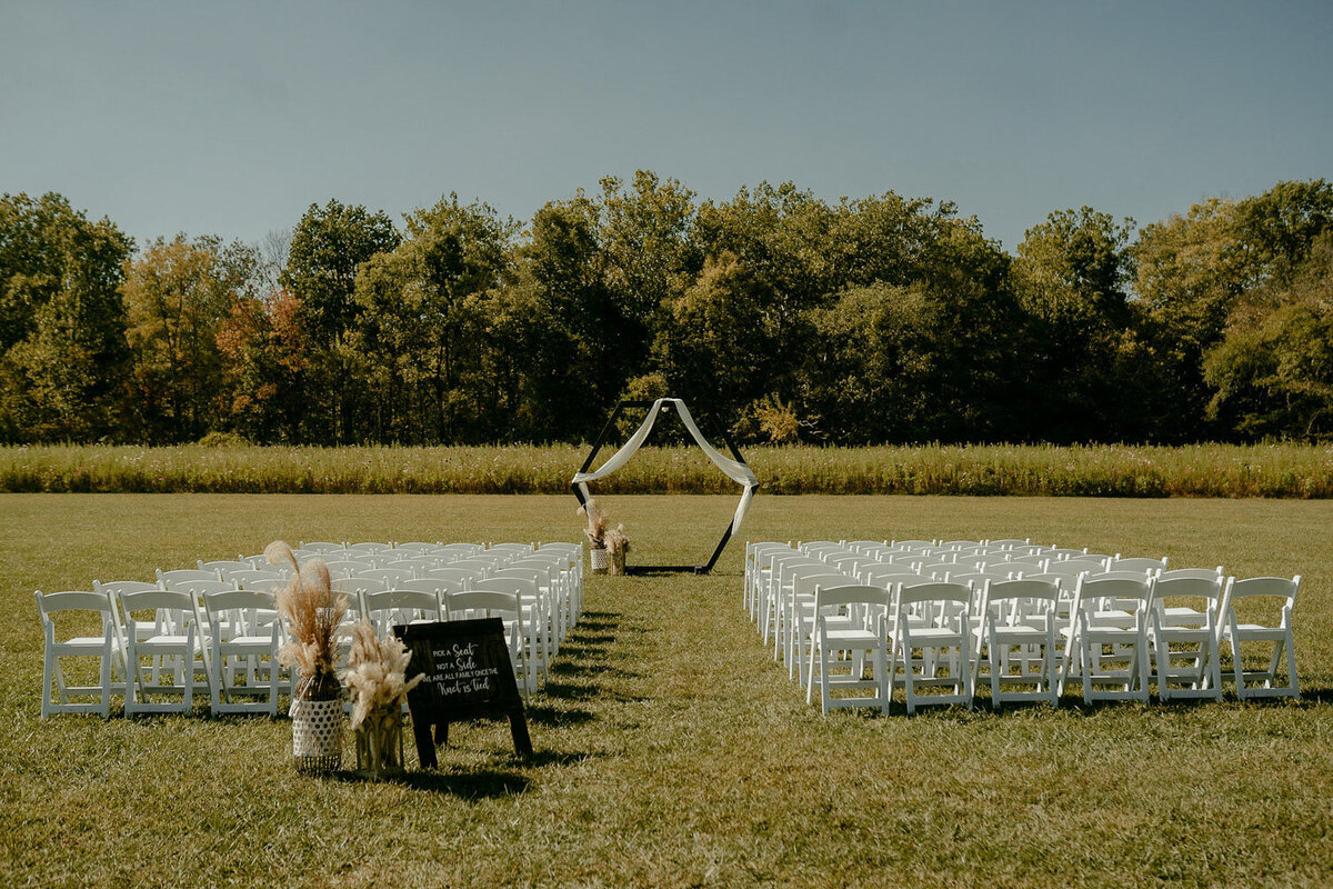 Outdoor ceremony setup with white chairs and a geometric arch