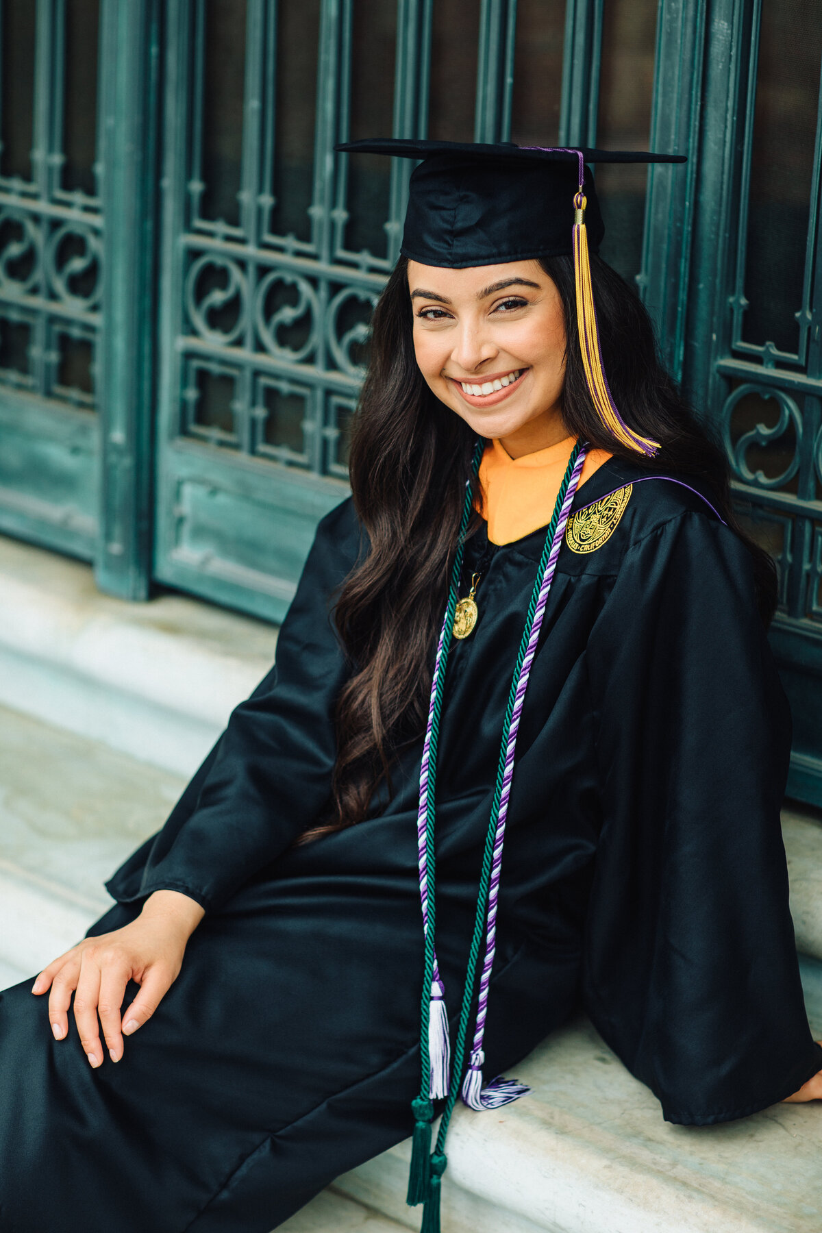 Graduation Portrait Of Young Woman In Black Toga Sitting  On a Cement Ground Los Angeles