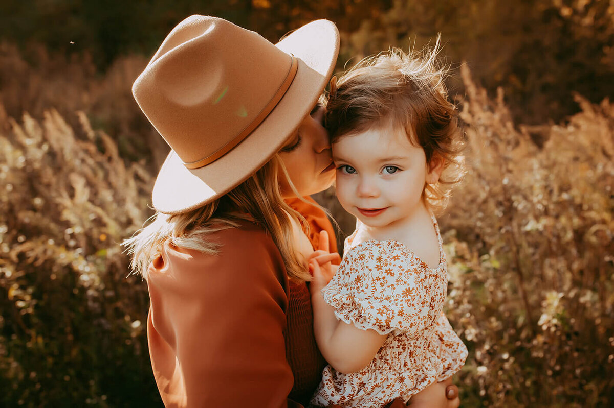 a mom kisses her little girls temple in a beautiful golden field