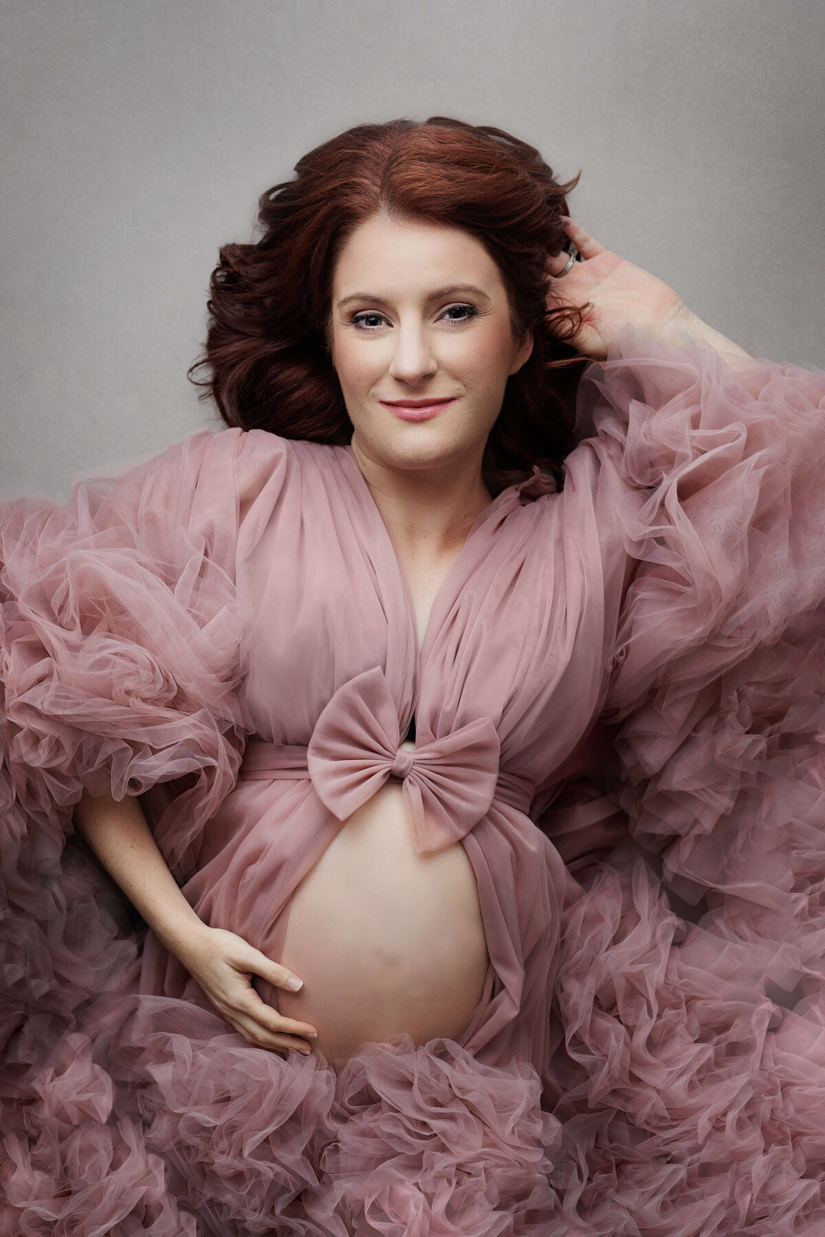 pregnant mother laying on her back with her baby bump showing wearing a fluffy maternity gown in pink at a photography studio