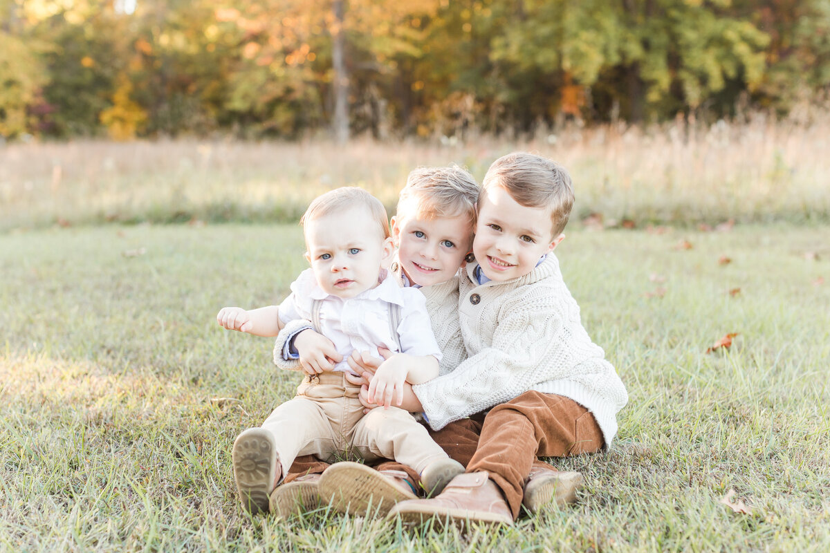 Three little toddler boys hugging while sitting on the ground by Northern Virginia Family Photographer