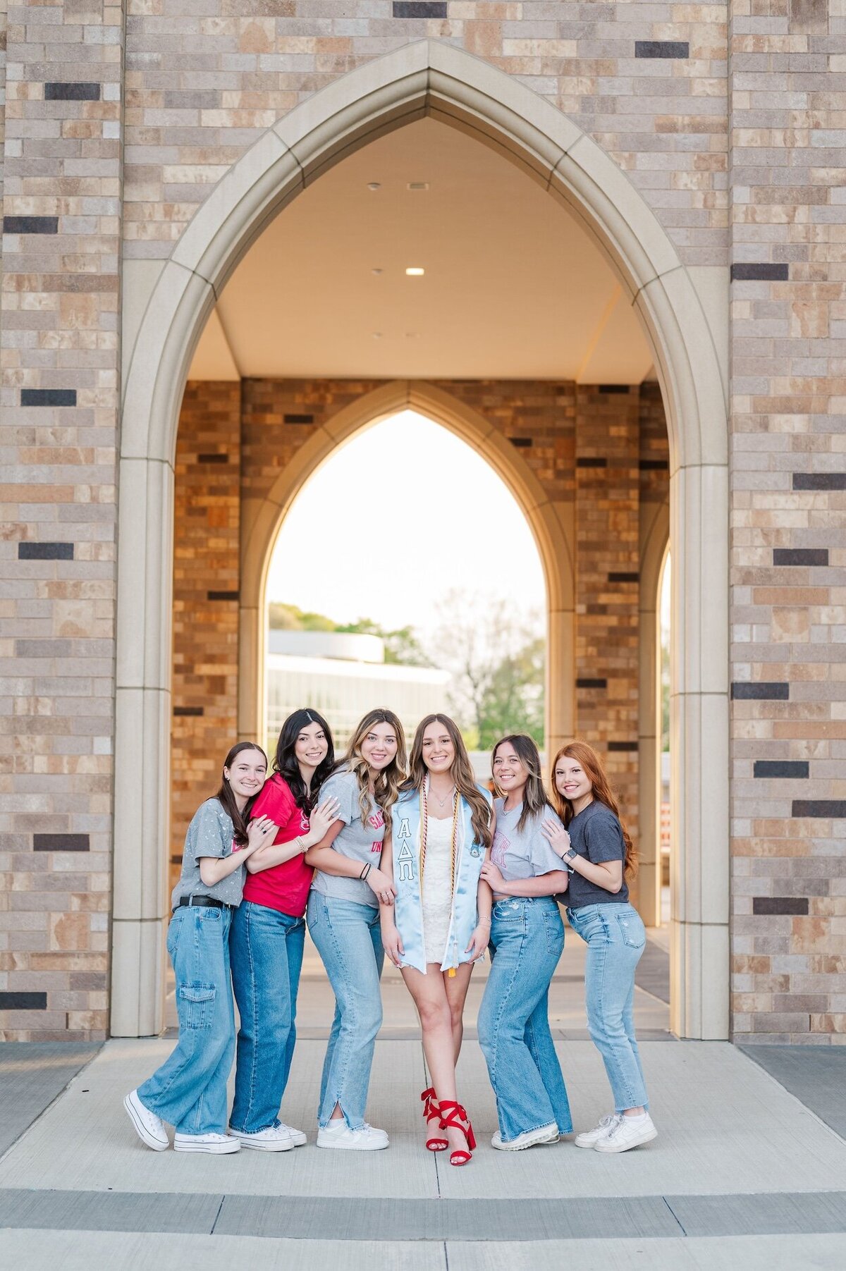 A sacred heart graduate and her five friends smile with one another under a popular arch on campus. 