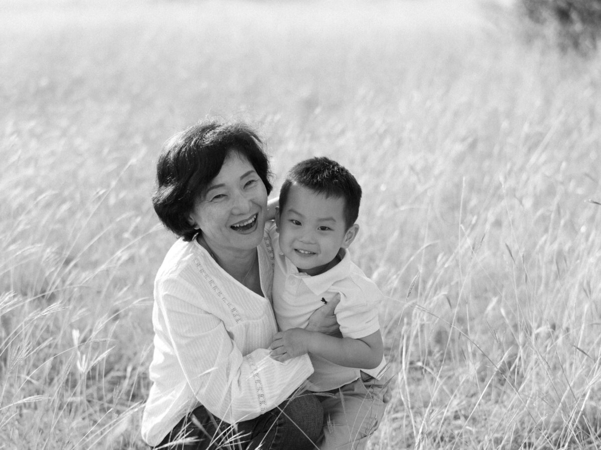 Black and white photo of grandma holding her grandson in a grassy field