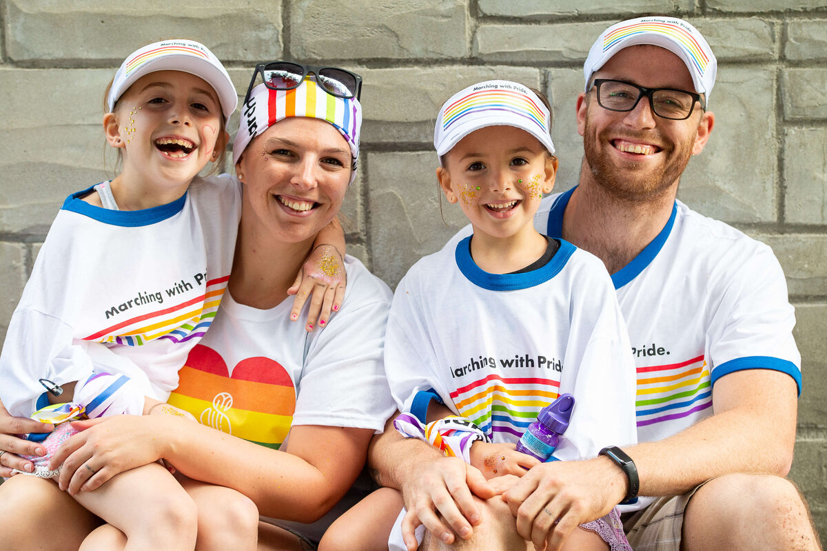 a family of four dressed in pride clothing laughing and smiling.  Captured by Ottawa Event Photographer JEMMAN Photography COMMERCIAL during the Tweed Canopy Growth Pride Parade