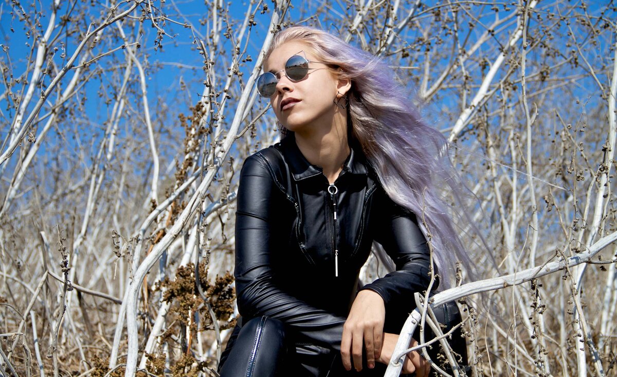 Women musician portrait Just Faith wearing black jump suit sitting in white reeds