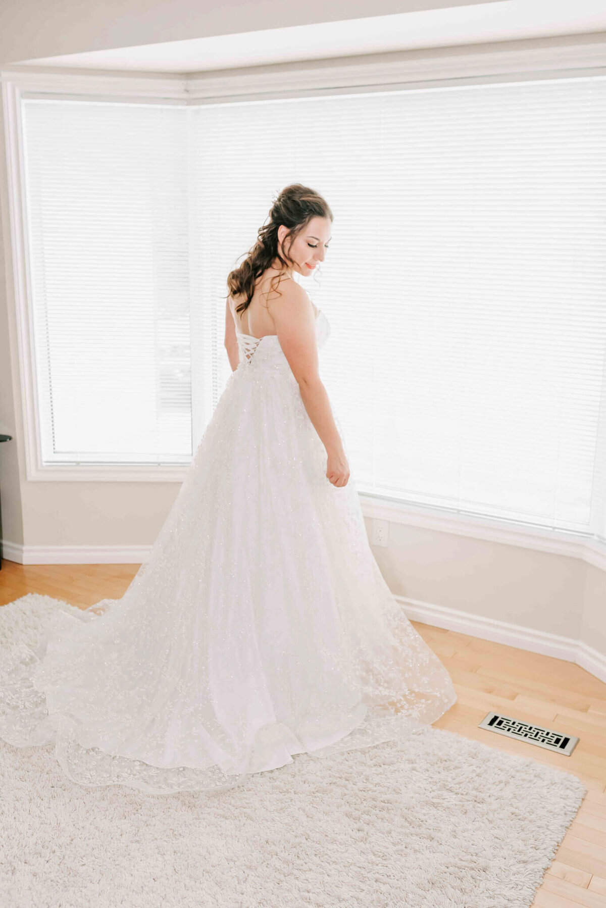 Bride stands in a window after getting into her dress. 