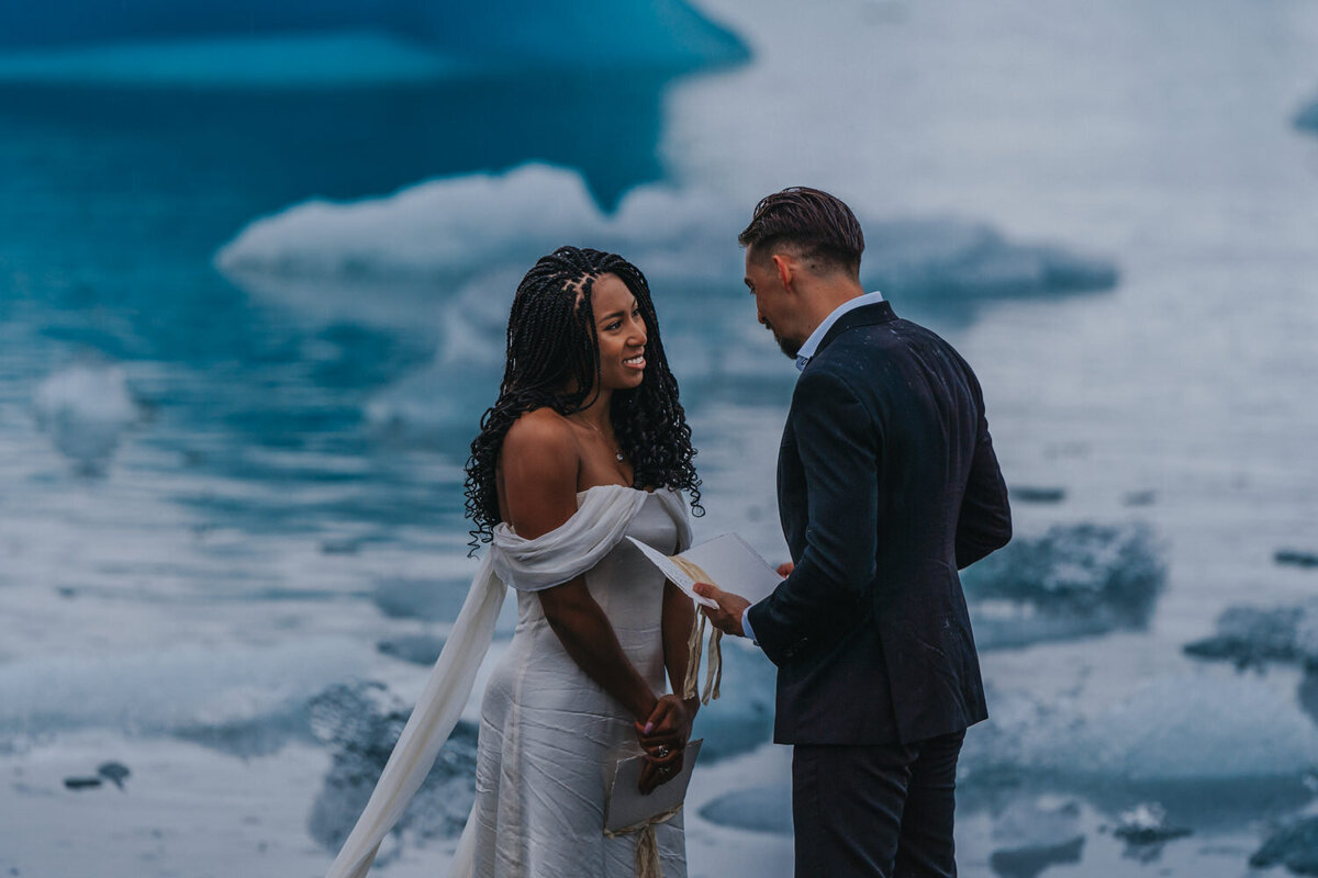 Against the stunning backdrop of Iceland's glacial lagoon, a couple smiles lovingly at each other during their intimate elopement ceremony 