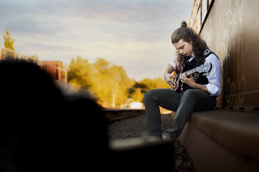 Senior portrait of a young man sitting near railroad tracks playing an electric guitar.