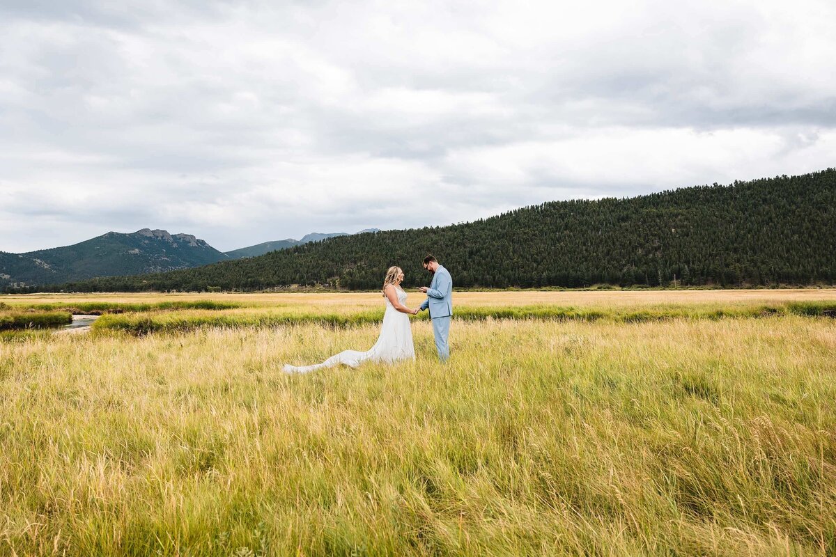 Couple Standing in Field With Mountain Backdrop