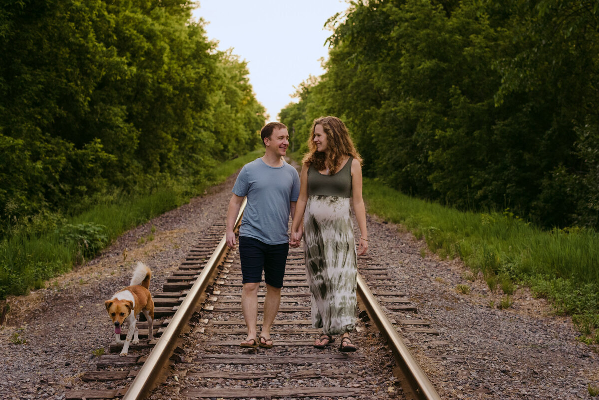 expecting parents walking along railroad tracks with their dog at sunset