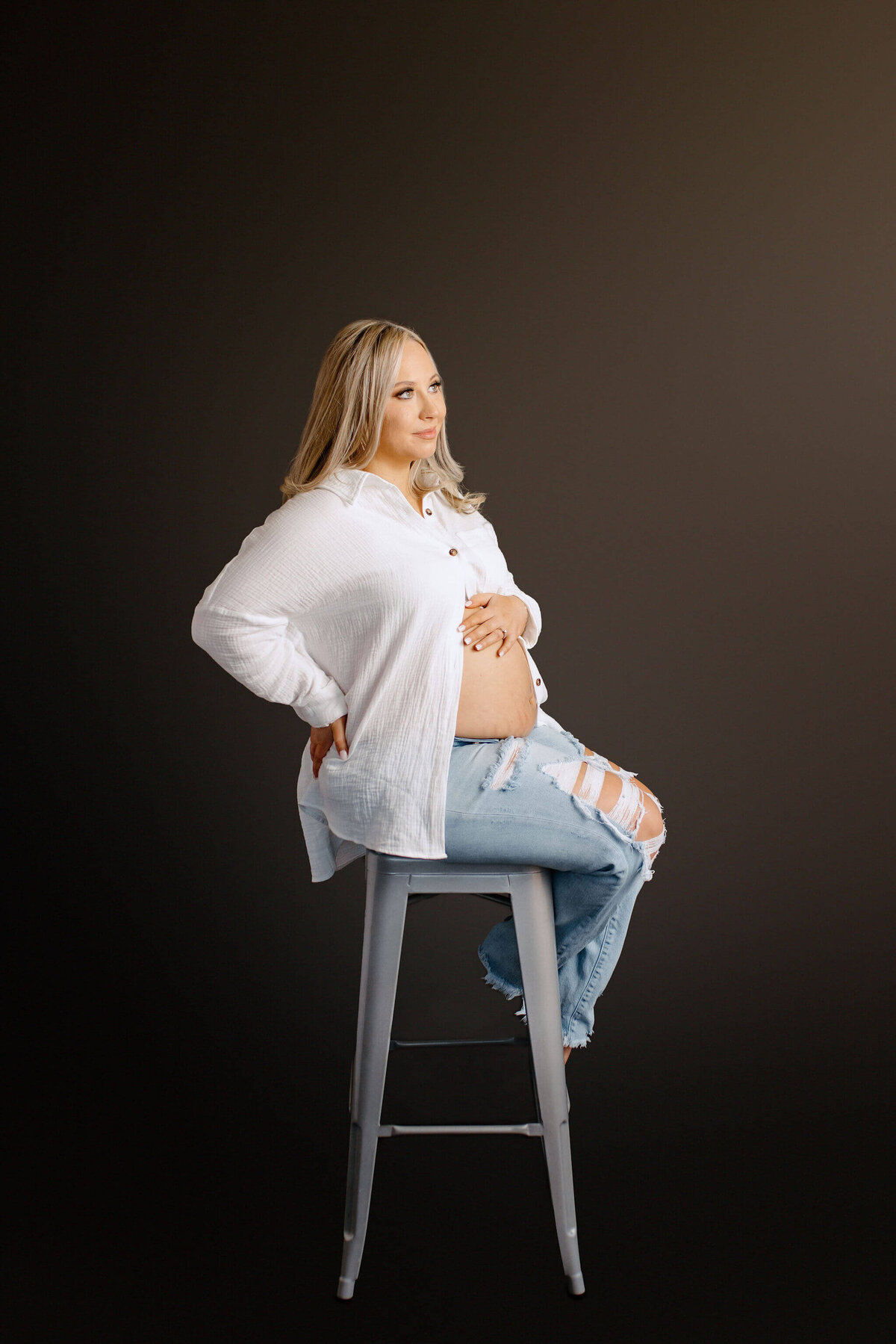 Studio style maternity photo of expecting mother sitting in stool