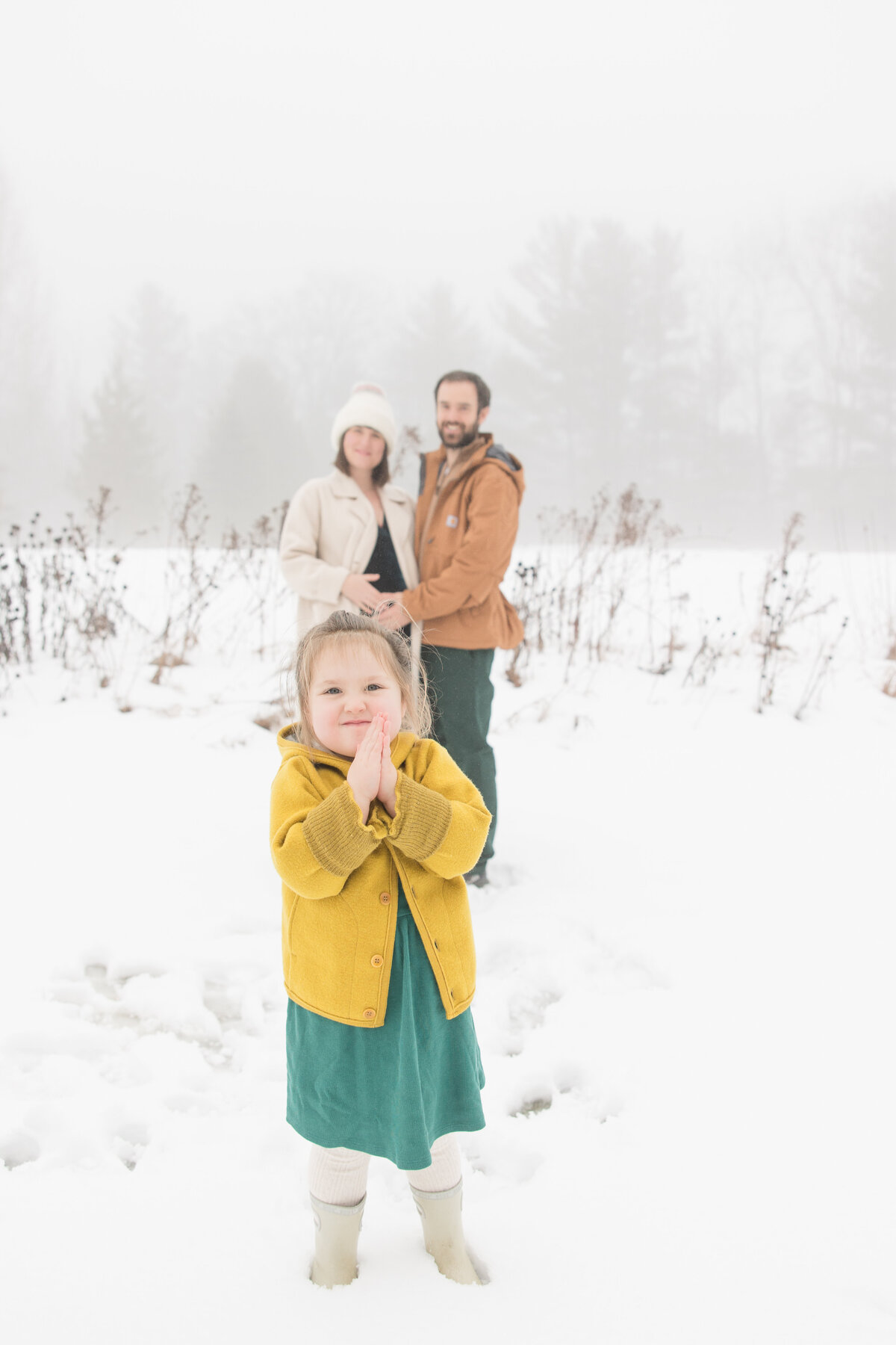 A little girl standing in front of her parents and smiling