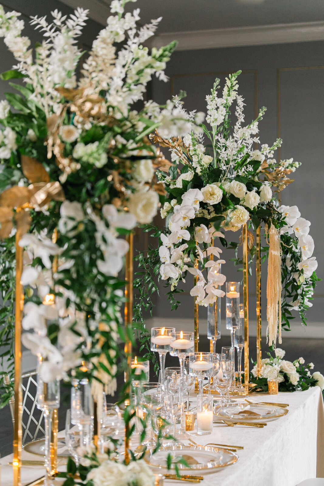 Luxury wedding reception floral details and table décor at The Thompson Hotel, featuring tall arrangements of white roses, orchids, amaranthus, gold stands, and candles.
