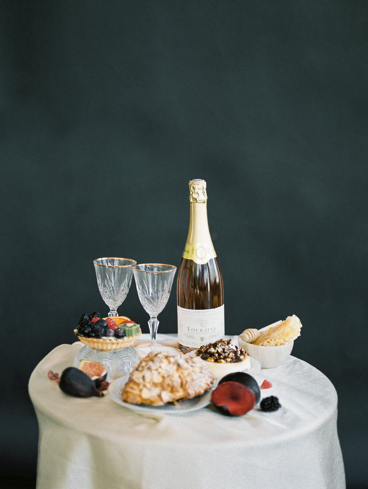 table with champagne, fruit, dessert with dark backdrop