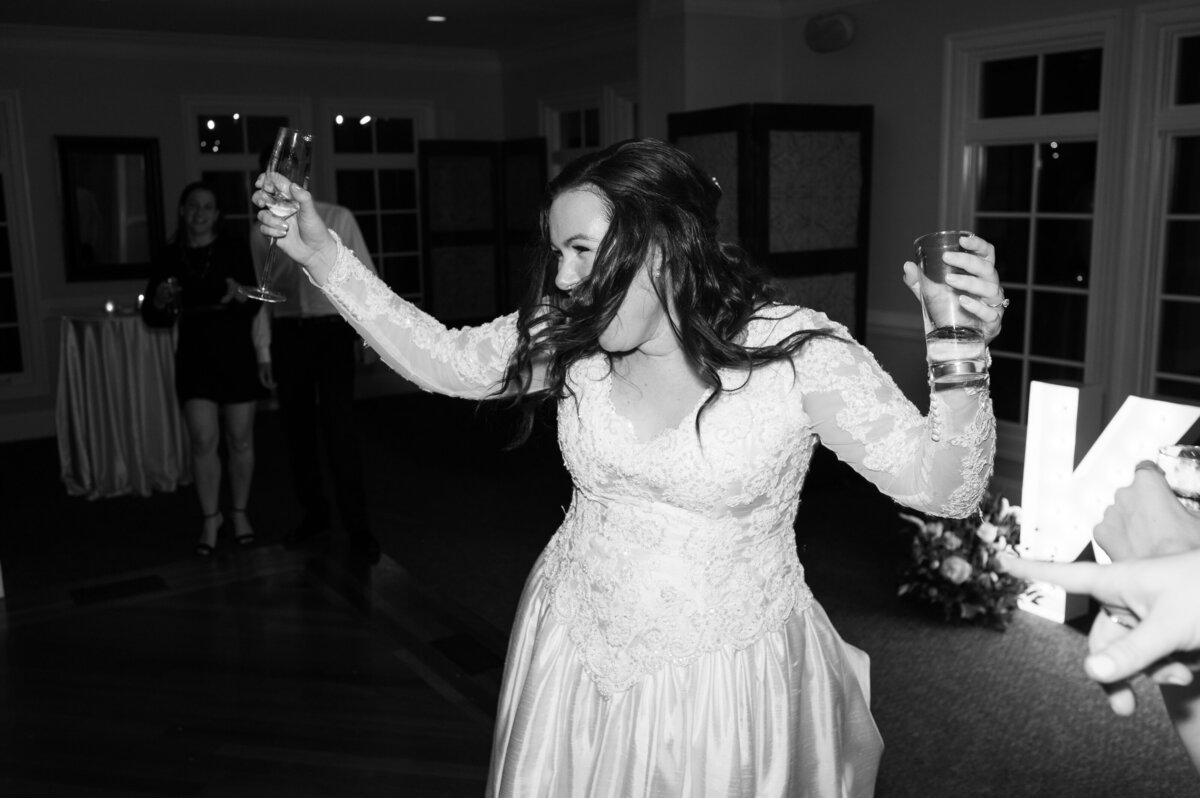 A bride holding drinks in both hands and dancing at her wedding reception