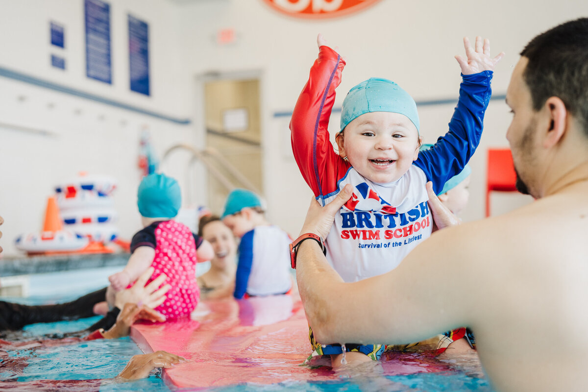 baby lifts arms in air during swim lessons