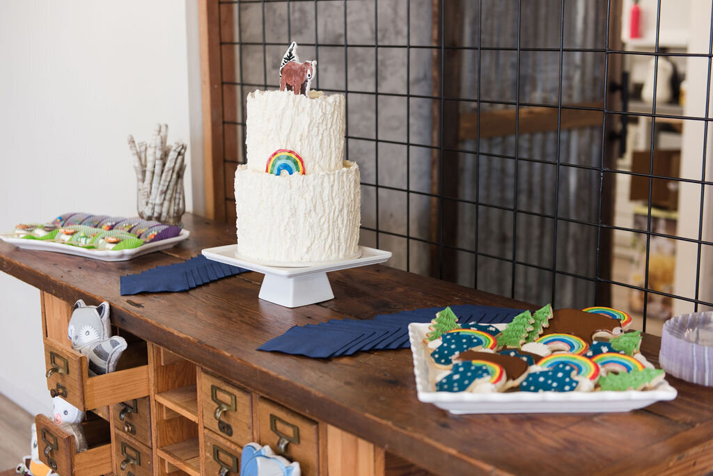 Dessert table at a woodland baby boy shower featuring a two-tier woodland-themed cake, custom cookies, and cake pops.