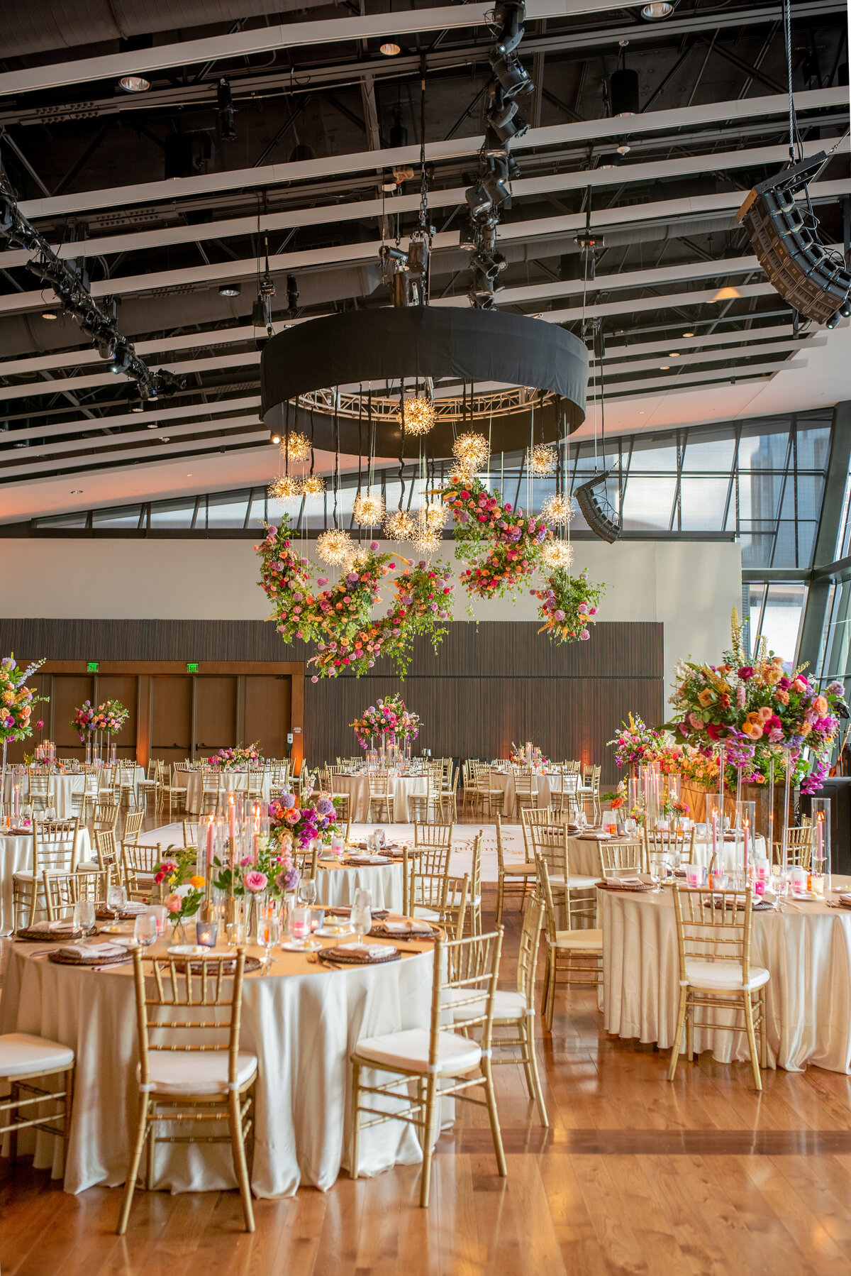 Joyful hanging floral cloud chandelier installation composed of petal heavy roses, allium, eremurus, delphinium, snapdragons, spray roses and garden-inspired greenery in hues of pink, fuchsia, lavender, orange, and golden yellow lighting up the dance floor of this summer wedding. Design by Rosemary and Finch in Nashville, TN.