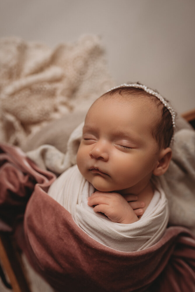 Newborn photo shoot photographed by Atlanta, Georgia newborn photographer with baby posing on neutral fabric with dainty headband on and sleeping.