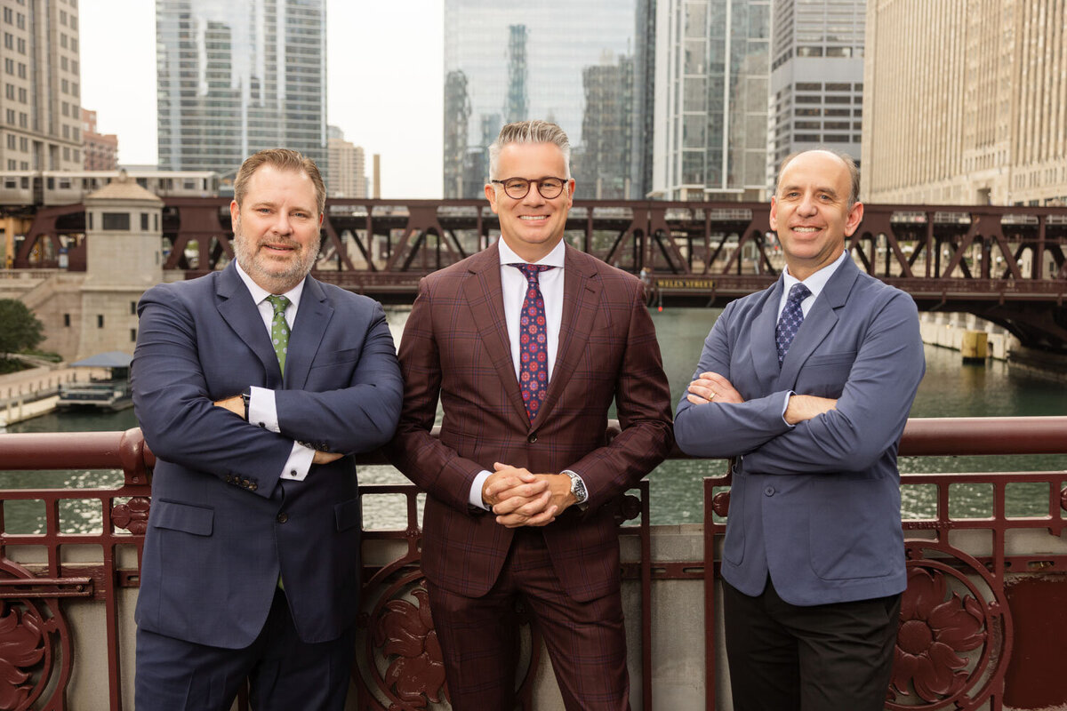 Three men in business suits standing by a city river bridge