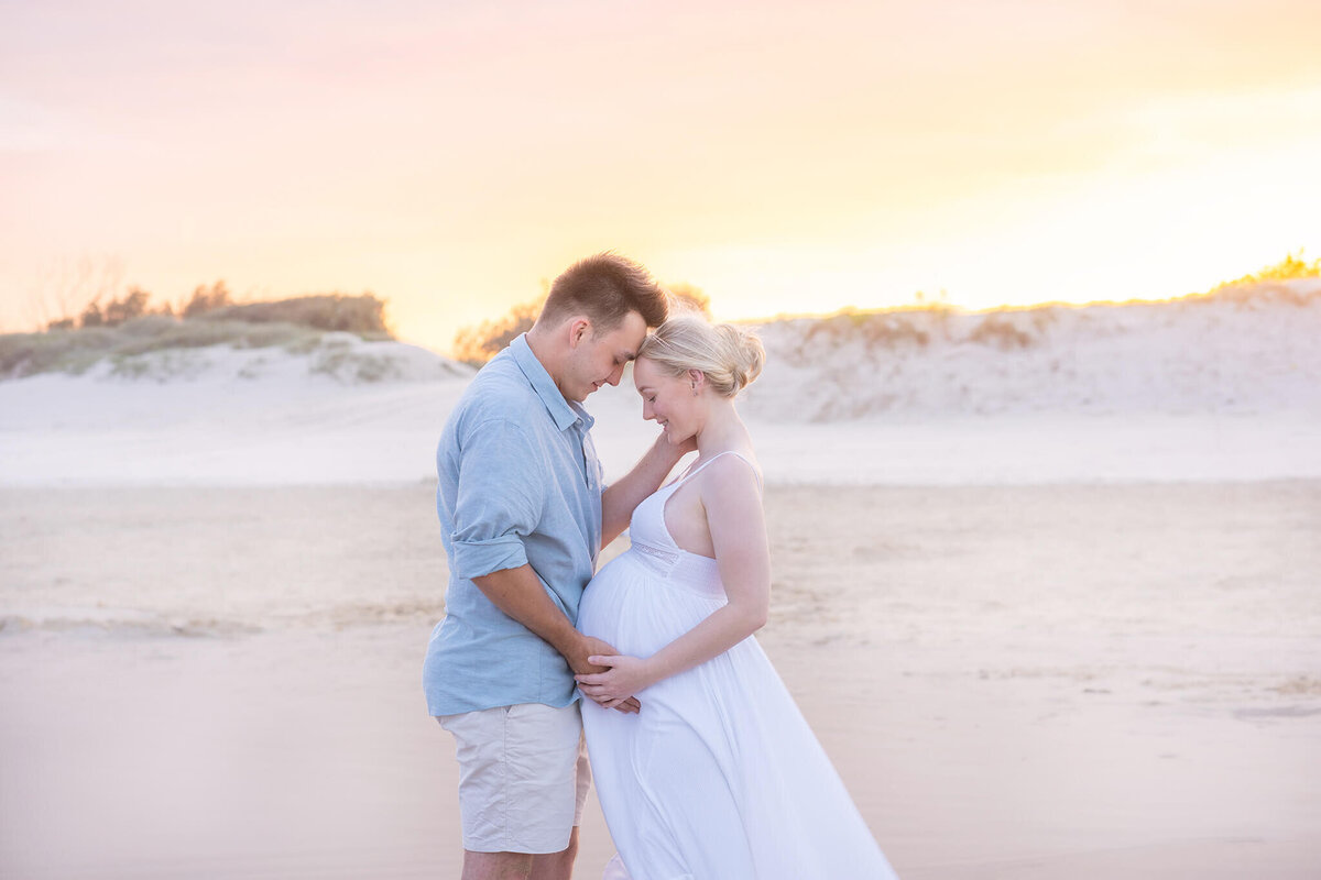 Couple touching belly bump during maternity photoshoot on the beach in Gold Coast