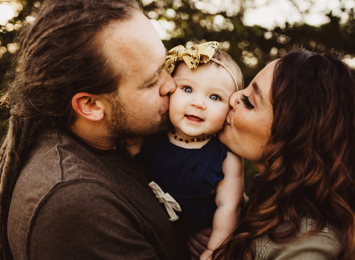 Mom and dad are kissing their smiling infant daughter.
