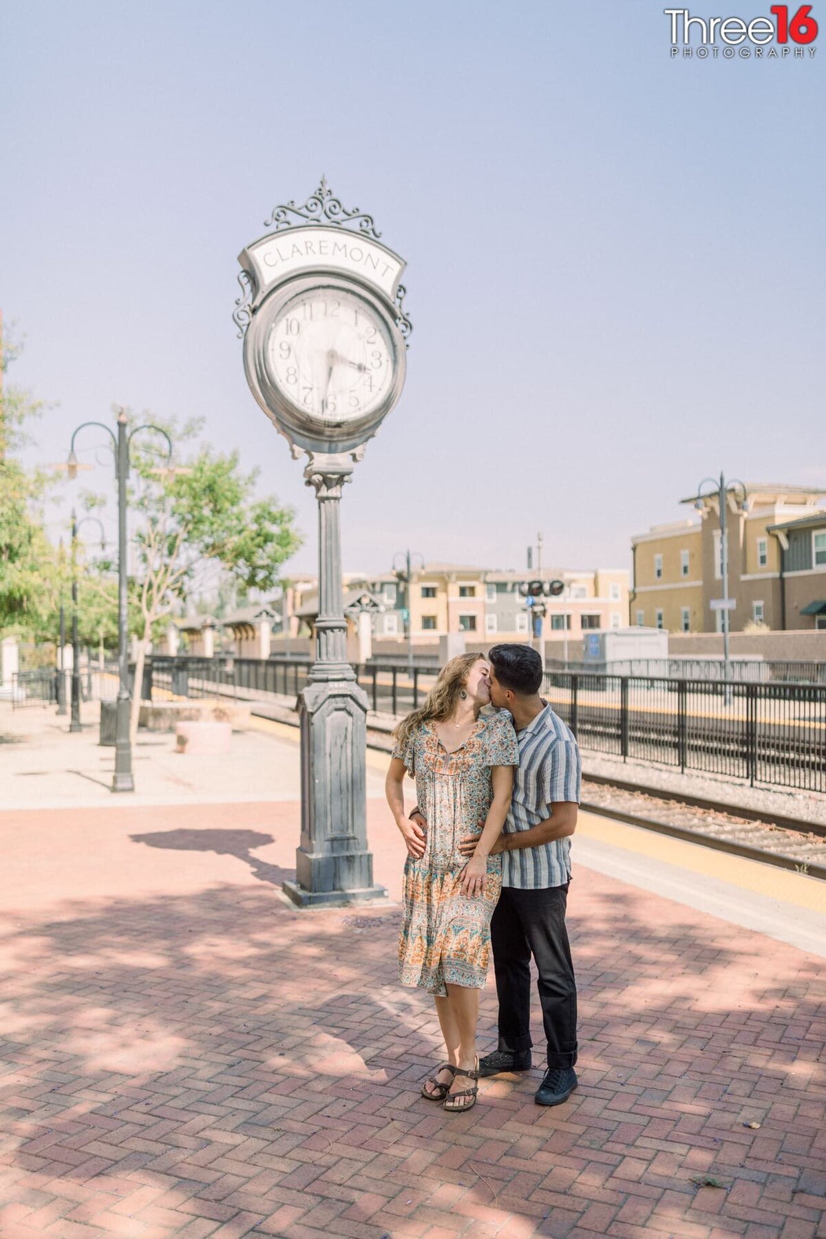 Bride to be looks back at her fiance and they share a kiss while standing under the Claremont Train Station clock tower